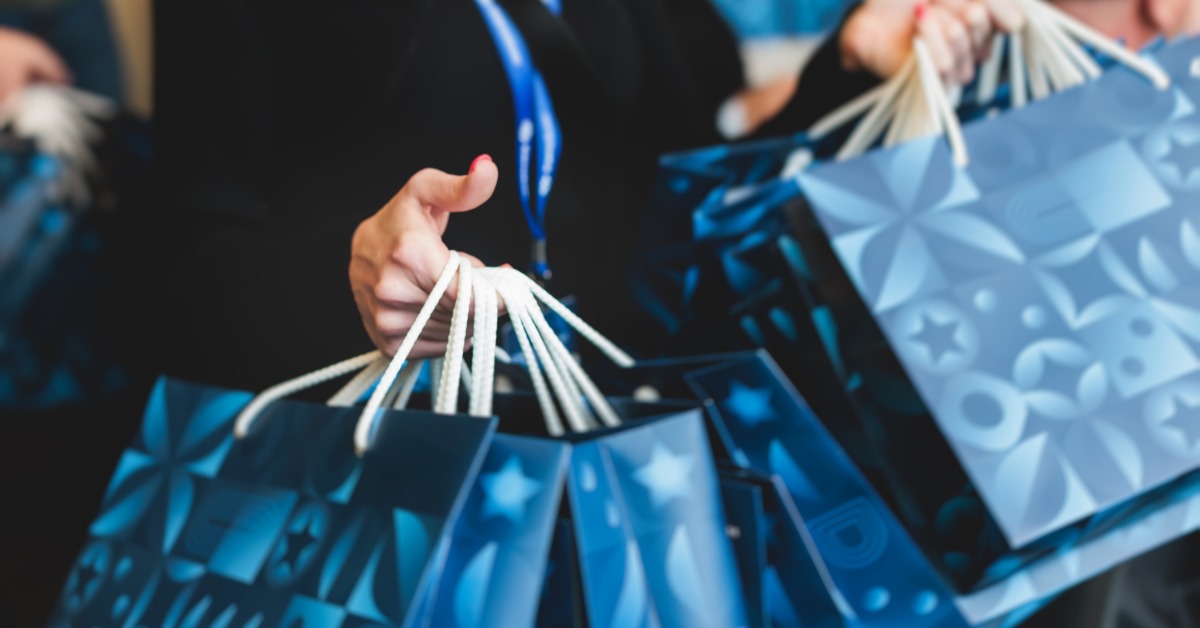 A trade show employee holding handfuls of gift bags with custom promotional products in the bag for attendees.