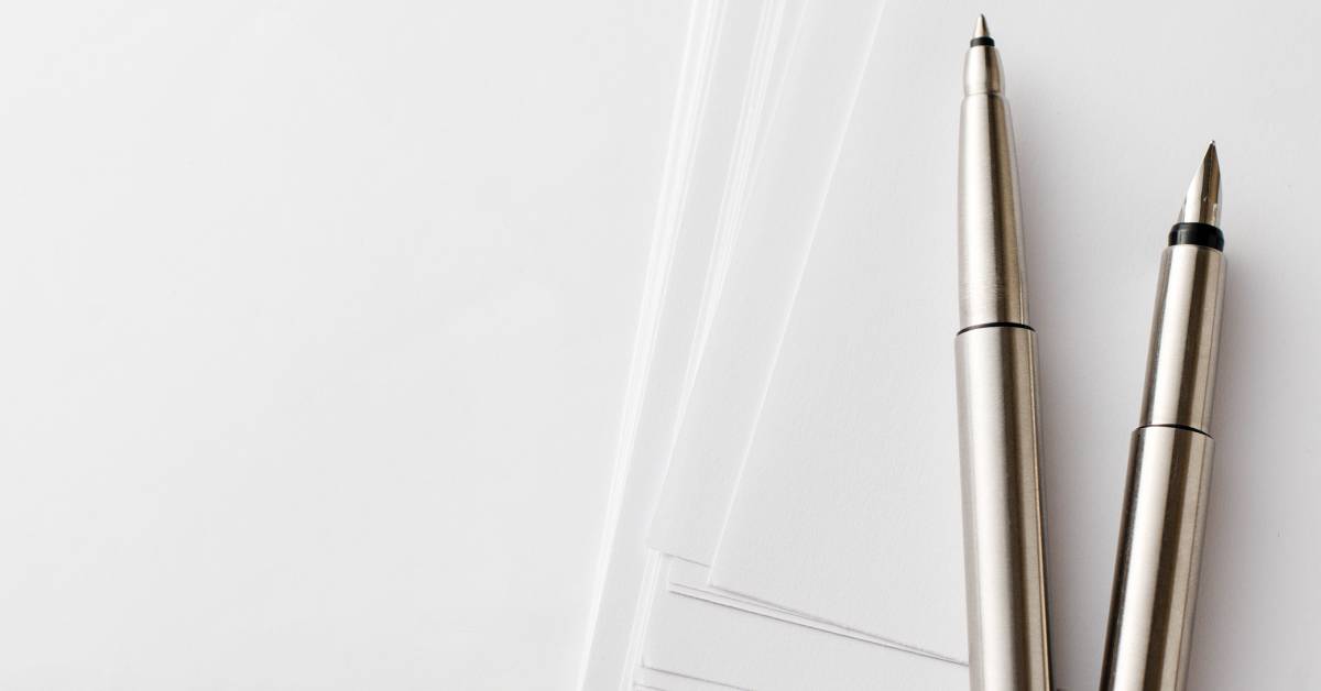 Two stainless steel pens sit on top of a stack of white papers. The pens are open, ready to write.