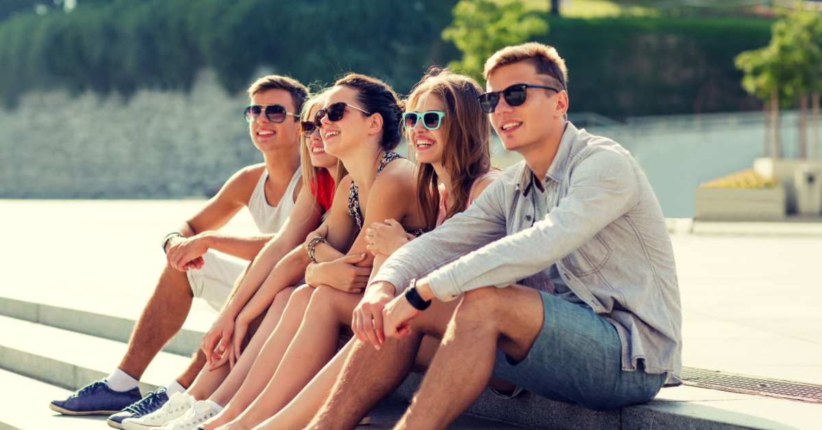 A group of five coworkers sit outside on the curb for a casual day of work. They all wear custom sunglasses.