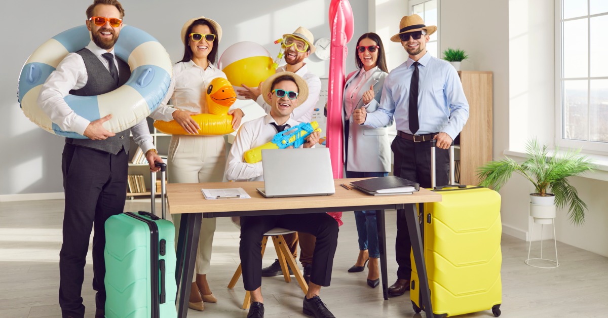 A group of office employees gathered around a workstation. They all have custom sunglasses and other summer items.