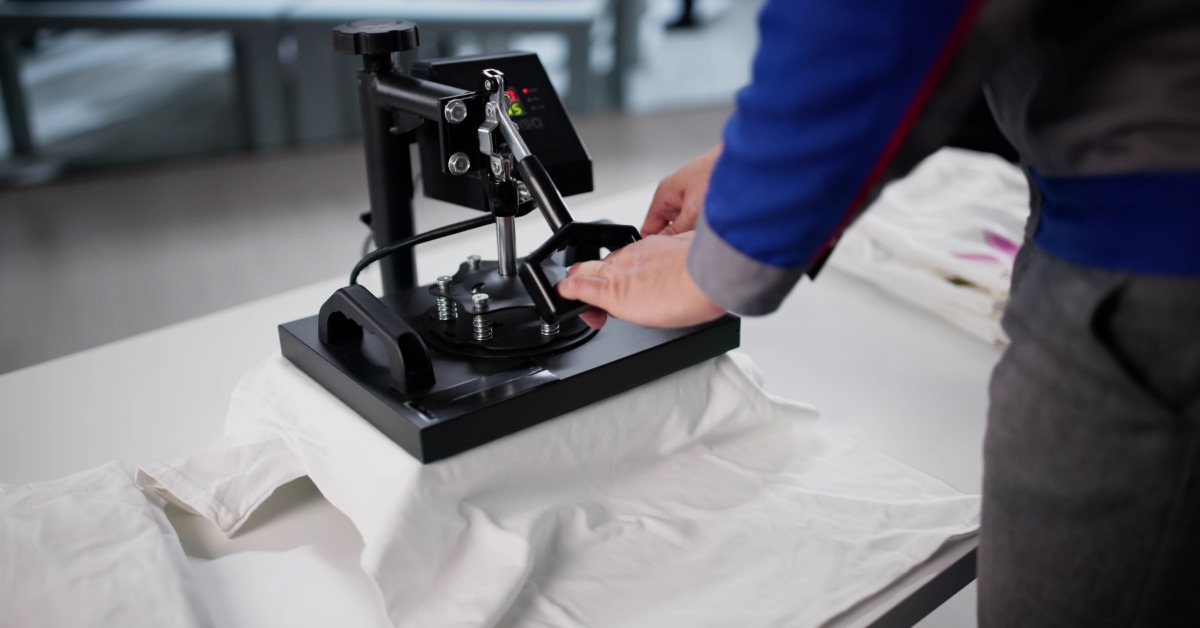 A professional stands at the screen print press as they wait for a white T-shirt to finish printing.
