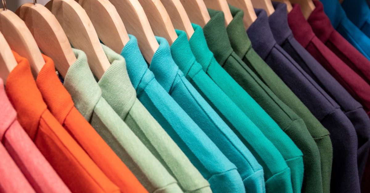 A row of colored polo shirts hang on wooden hangers. The row is color coded and the shirts are plain.