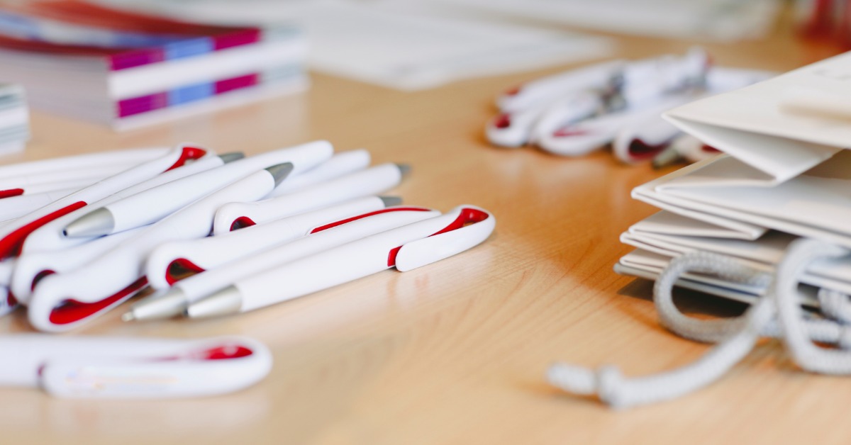 A pile of company logo pens sits on a desk at the office. The pens are custom for the new hire welcome kits.