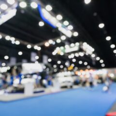 A blurry view of a convention hall with a trade show taking place The lights are bright and there is blue carpet