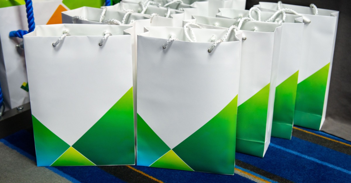 A group of giveaway bags at a corporate conference. The bags are white with a blue and green design.