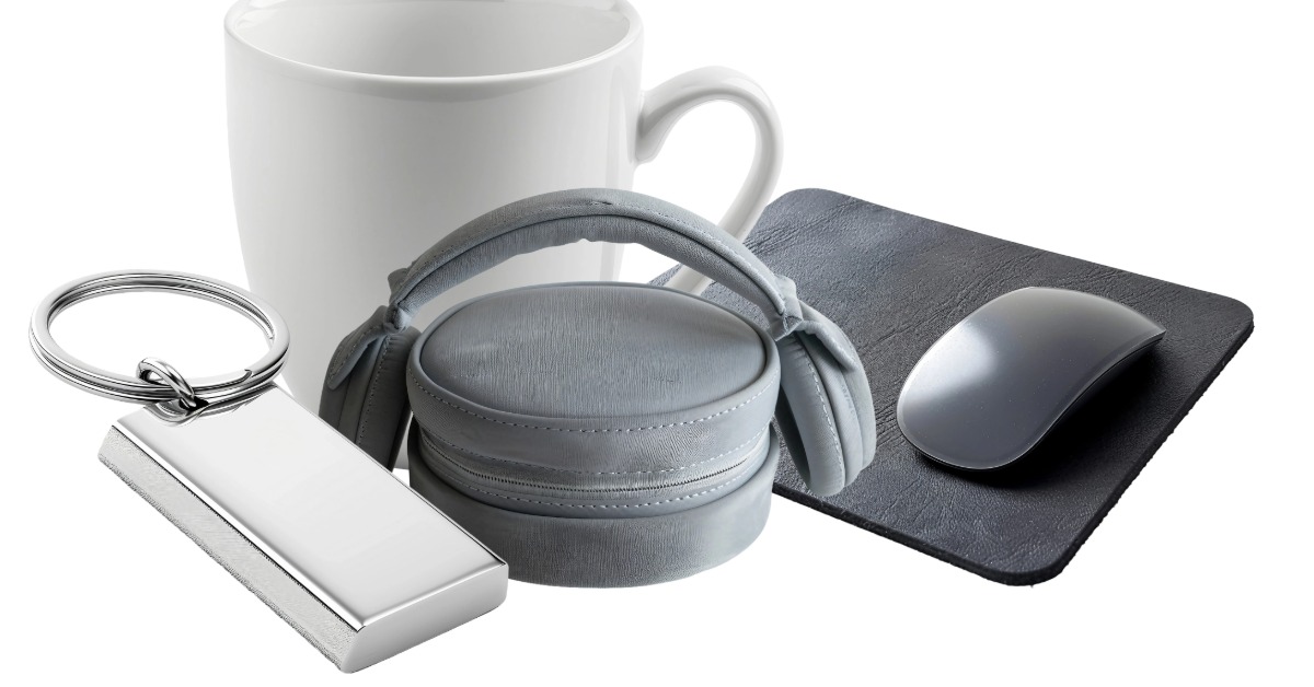 A pile of promotional products sit on a white surface. The items include a mouse pad, coffee mug, keychain, and headphones.