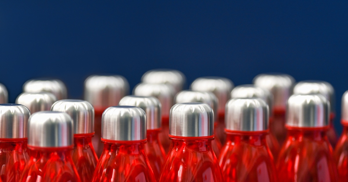 A close-up of a collection of red water bottles sitting on a table against a navy blue backdrop. The bottles have steel lids.