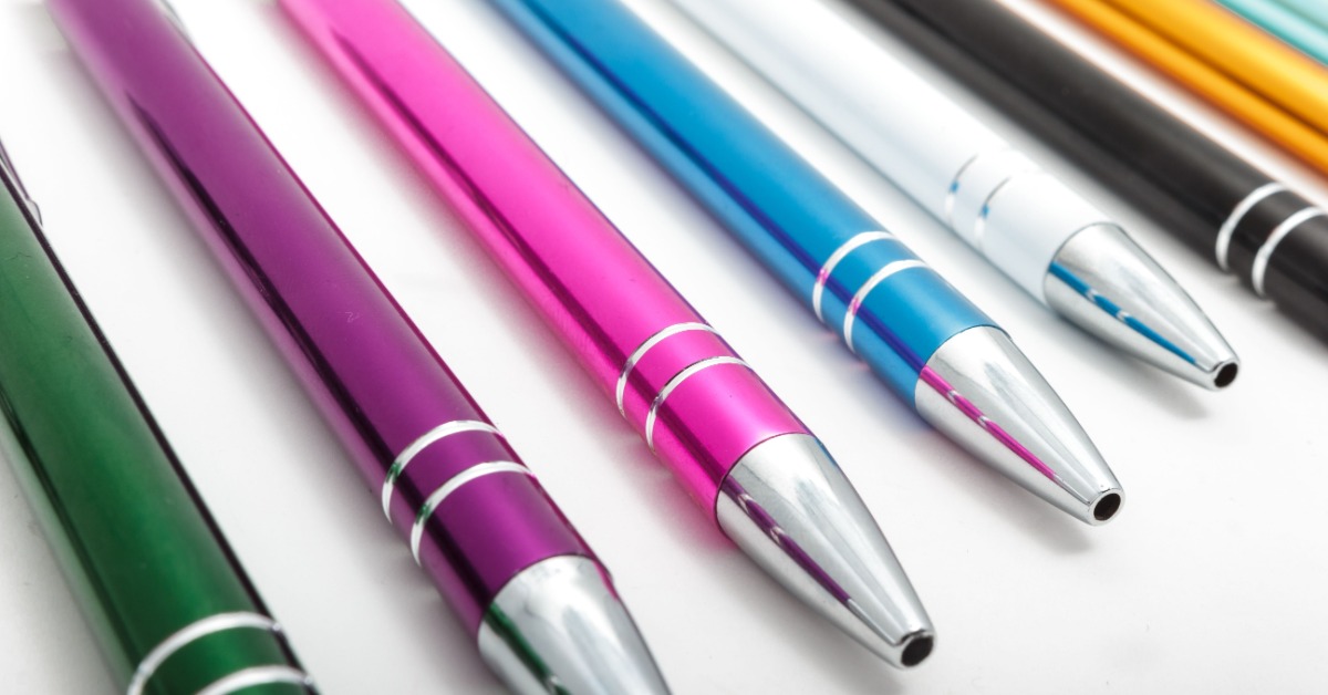 A close-up of a collection of ink pens. They are metal metallic in a variety of colors: green, purple, pink, and blue.