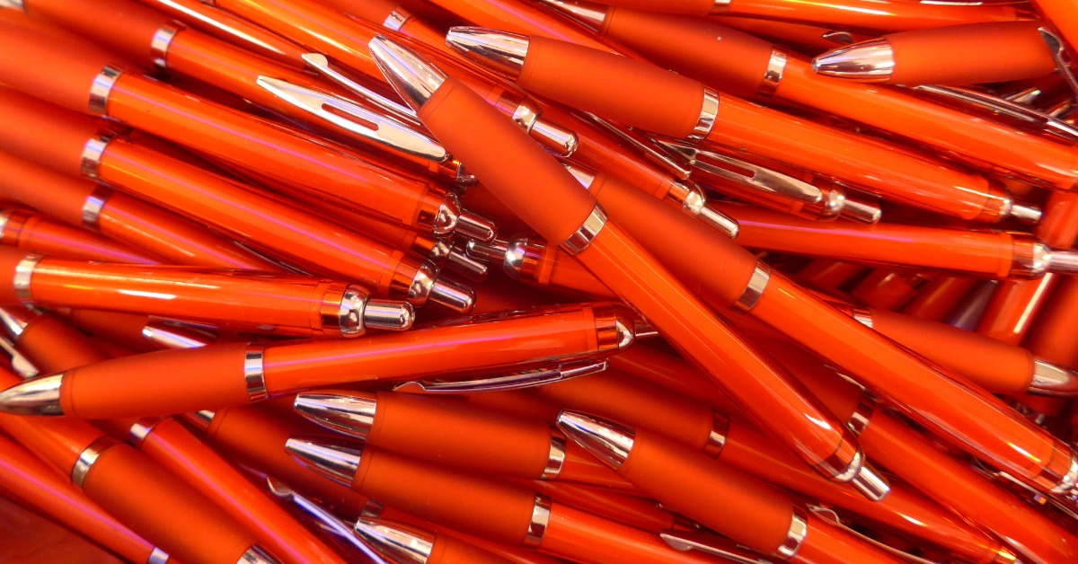 A pile of red pens thrown together on a tabletop. The pens have nice red bodies with silver accents.
