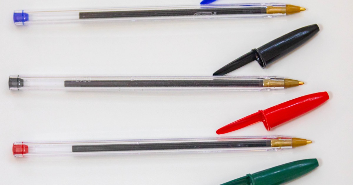Four traditional ink pens on a white surface. The caps are off and each a different color: blue, black, red, and green.