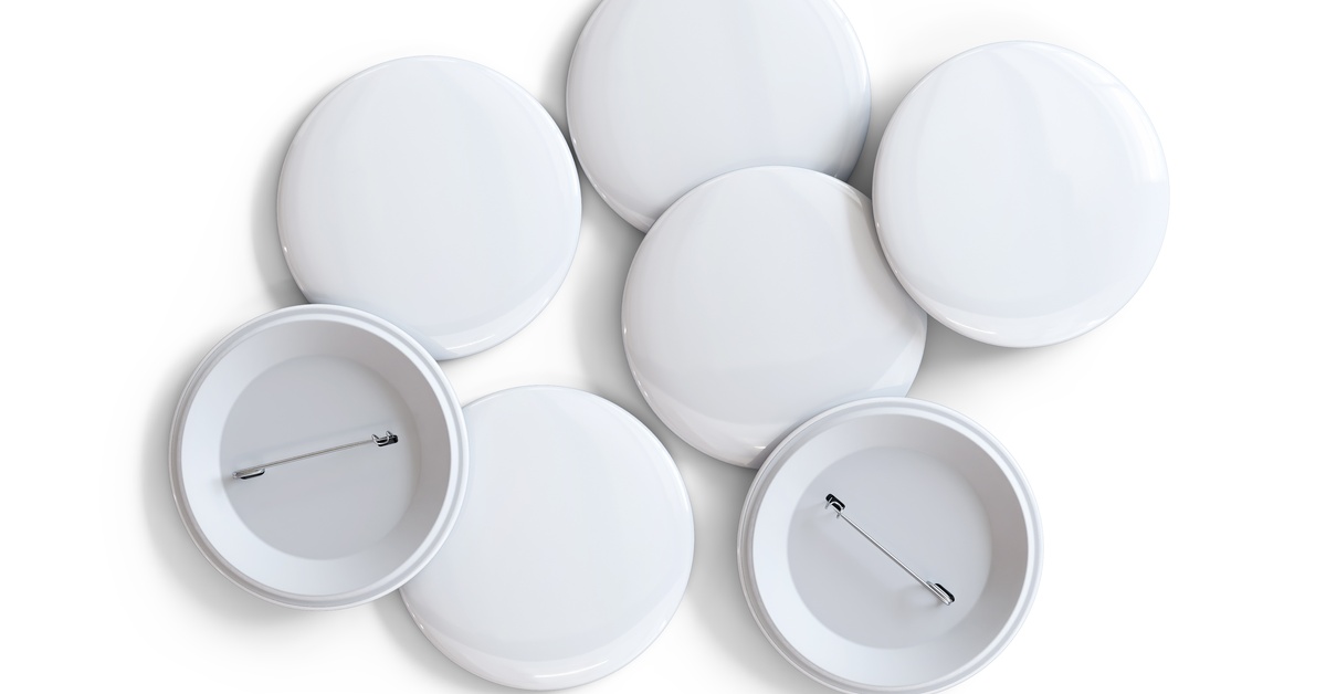 A collection of plain white button pins. Some of the pins are face up and some of them are pin-side up.