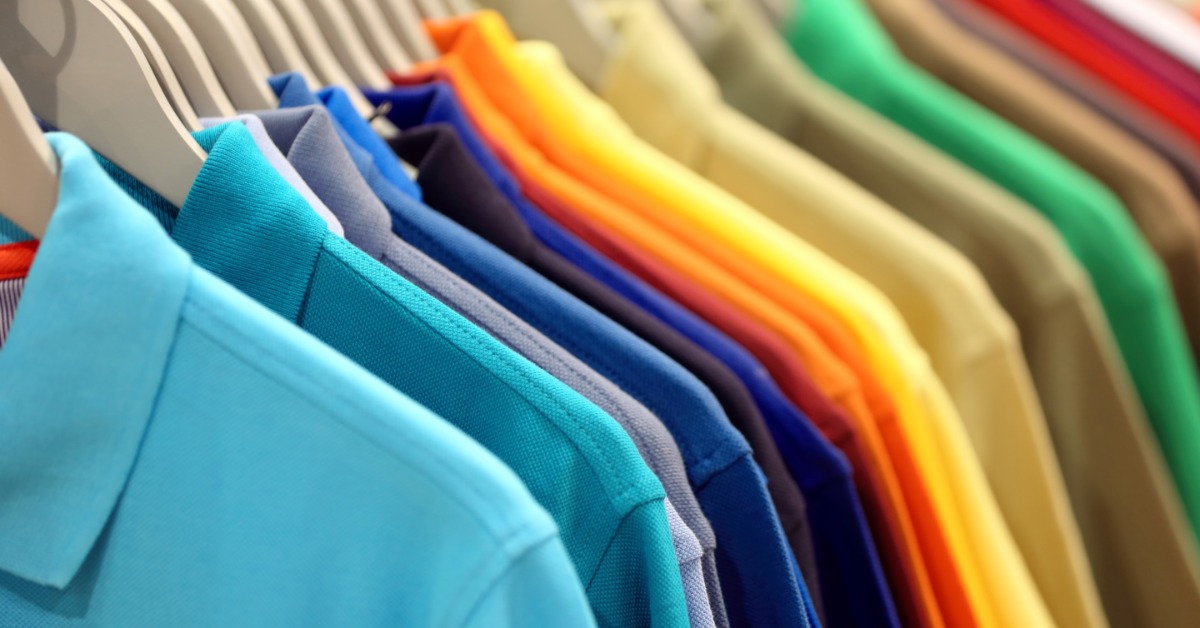 A close-up of a row of hanging polo shirts. The polos are a range of colorways, such as blue, yellow, orange, and green.