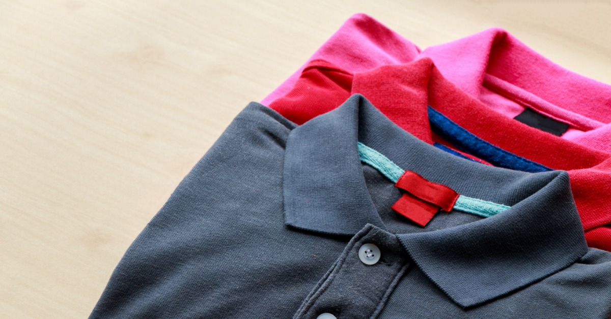 Three polo shirts folded neatly on the table. The polo shirts are buttoned and in colors black, red, and pink.
